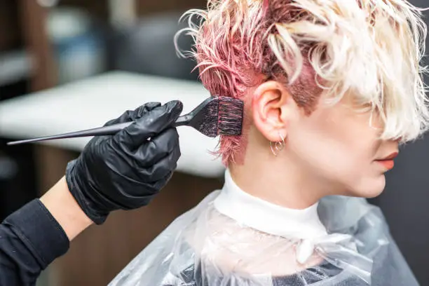 Photo of Hairdresser hand in black gloves paints the woman's hair in a pink color.