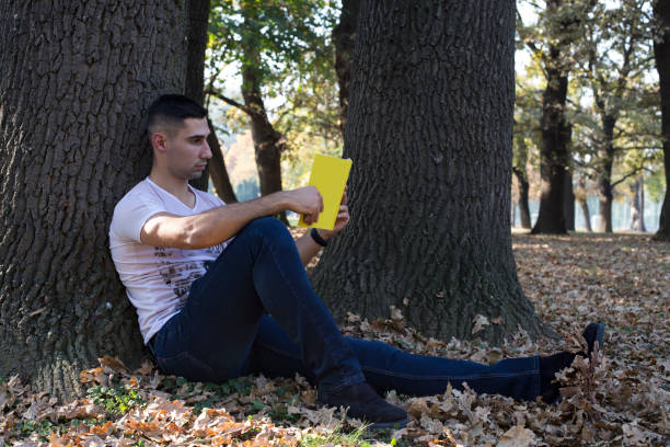 istock Young relaxed man reading book in nature 1182132644