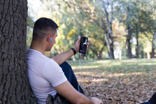 istock Man with headphones resting under tree in park 1182133960