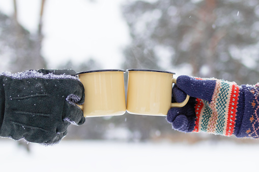 Two metal cups with hot tea in hands man's and woman's on a background of winter forest.