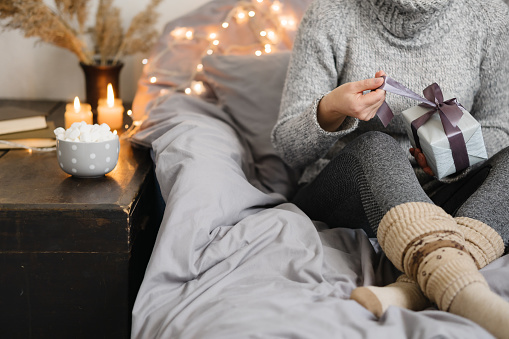 Woman holding gift in cozy room. Cold day in warm house. Concept Hygge. Merry Christmas!