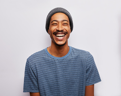 Studio portrait of a young man wearing a t-shirt and hat laughing against a gray background