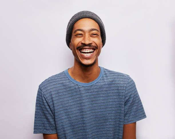 Laughing young man standing against a gray background Studio portrait of a young man wearing a t-shirt and hat laughing against a gray background hipster culture stock pictures, royalty-free photos & images