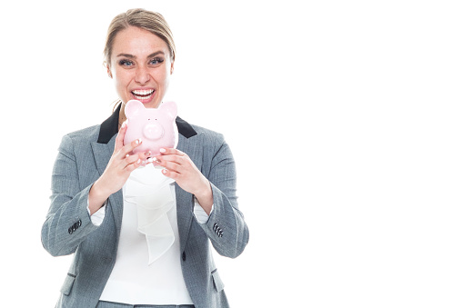 One person / front view / waist up of 20-29 years old adult beautiful caucasian female / young women businesswoman / business person standing in front of white background wearing a suit who is smiling / happy / cheerful / successful and holding piggy bank / currency / investment / retirement / savings / wealth