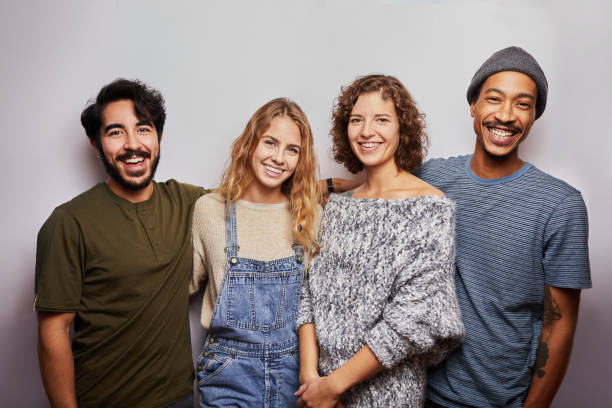 Smiling group of diverse young friends against a gray background Studio portrait of a diverse group of a smiling young friends standing arm in arm together against a gray background diverse models stock pictures, royalty-free photos & images