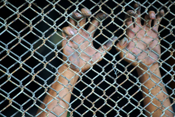 Human hand is holding on wire mesh fence.