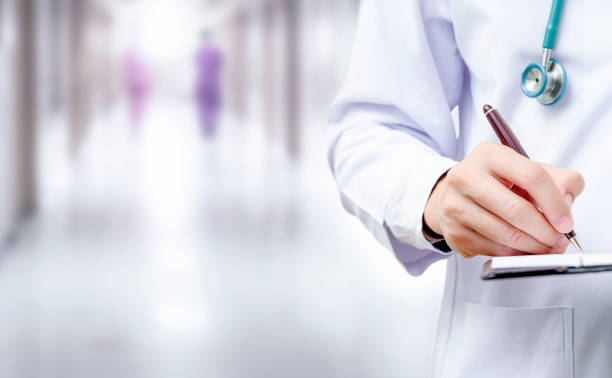 istock doctor hand writing on application form while standing at hospital. 1182154892