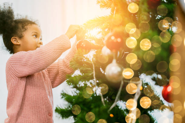 afrikanische weibliche kind arrangieren schmücken weihnachtsbaum mit spaß und fröhliche weihnachten festliche ideen konzept - christmas family child christmas tree stock-fotos und bilder