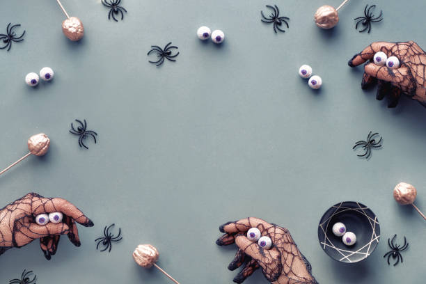 istock Creative Halloween flat lay in grey, pink and black with decorative pumpkins and spiders. Hands in black mesh gloves imitating monsters. Grey paper Halloween backdrop with copy-space 1182169423