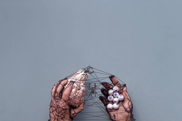 istock Creative Halloween flat lay in pink and black on gray paper with copy-space.  Hands in black mesh gloves holding pink pumpkin and handful of chocolate eyes. 1182171012