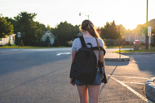 Profile of a teen girl depressed at sunset in a parking lot while wearing a backpack.