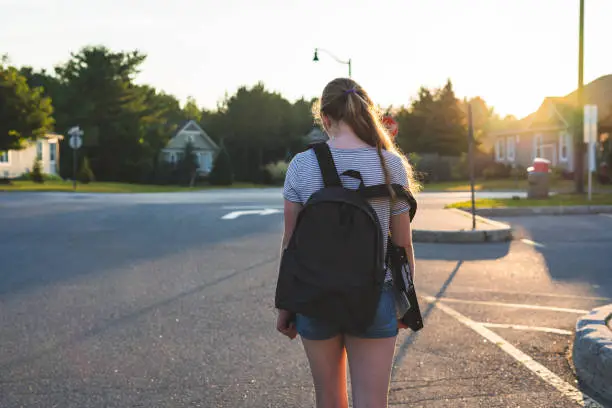 Photo of Profile of a teen girl depressed/sad at sunset in a parking lot while wearing a backpack.