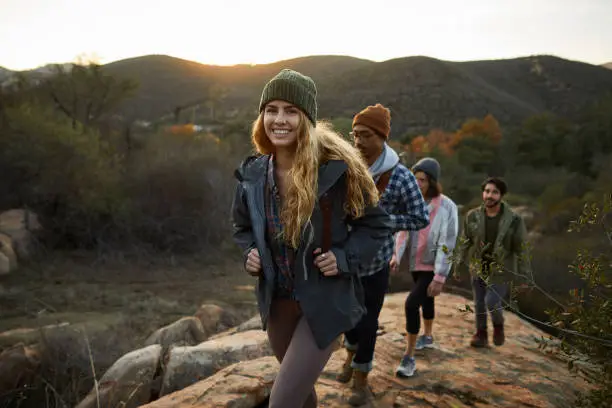 Smiling young woman and friends walking up a rocky path during an early morning hike together in the hills