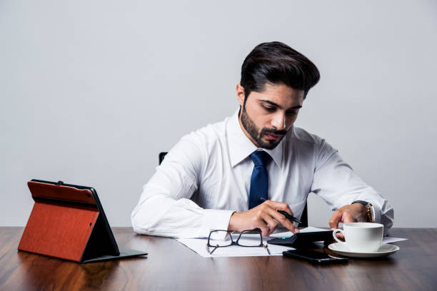 オフィスの机/テーブルに座っている間、ひげを生やしたインドのビジネスマンの会計 - manually ストックフォトと画像