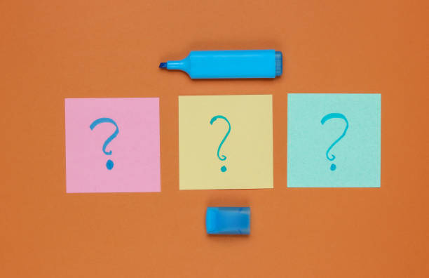 istock Memo pieces of paper with drawn question marks, felt-tip pen on brown background. Top view 1182181798