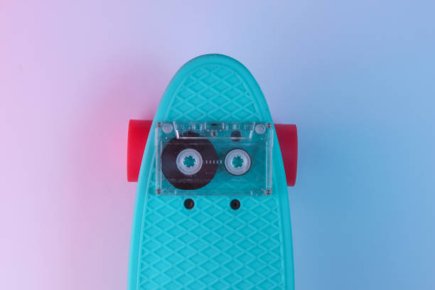 istock Plastic mini cruiser board and audio tape on background with blue pink neon gradient ligh. Top view 1182183033