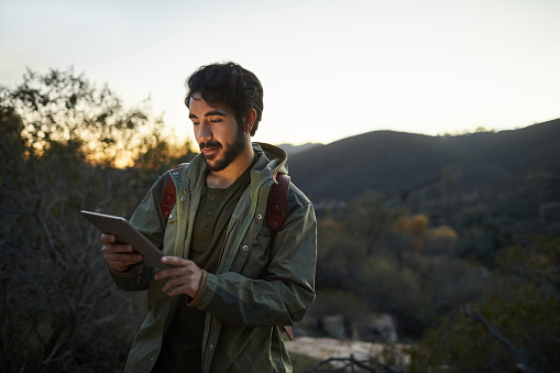 Young man wearing a backpack using the gps on his digital tablet while out for an early morning hike