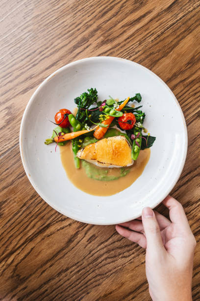 istock Pan seared Cod fish fillet with tomato, bean and carrot in gravy sauce. Served in white plate with hand touching. 1182184474