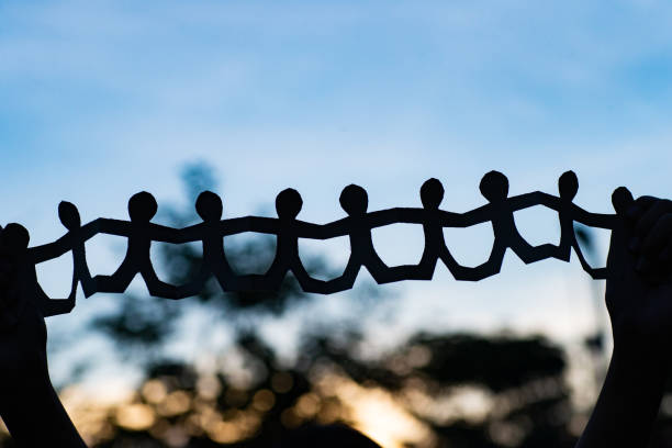 gruppe von papiermenschen, die bei sonnenuntergang die hände auf die natur halten. - unity paper chain holding hands paper stock-fotos und bilder