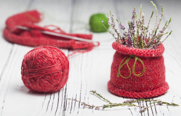Knitting as a hobby. A large red ball of red thread.Flowers in a knitted vase.