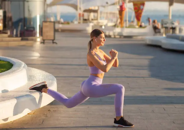 Morning workout concept. Young fit woman in sportswear doing lunges exercise at sunrise outdoors