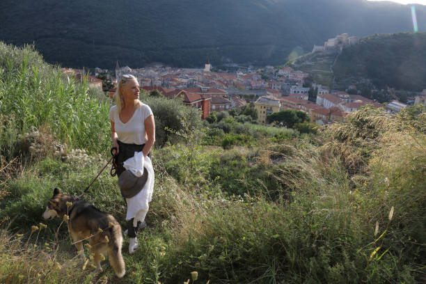 mujer madura camina perro a través de la ladera - people personal accessory town hat fotografías e imágenes de stock