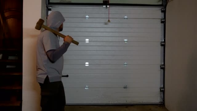 A man with a sledgehammer and a hood is standing in the garage 4K