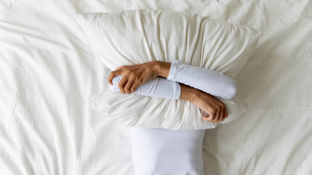istock Young girl lying on bed, covering face with pillow. 1182206031