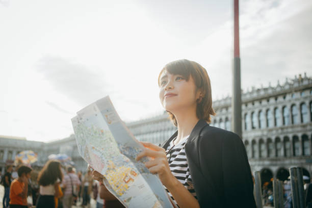 istock Young Asian female traveller reading map while exploring and walking through local city street in Italy 1182206175