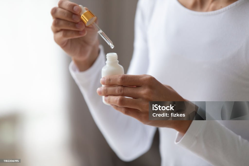 Close up young woman holding bottle with pipette. Close up young woman holding bottle with pipette, using coconut moisturizing oil or pleasant fragrance liquid. Lady opening container with medical cosmetic product, beauty procedure at home. Skin Care Stock Photo