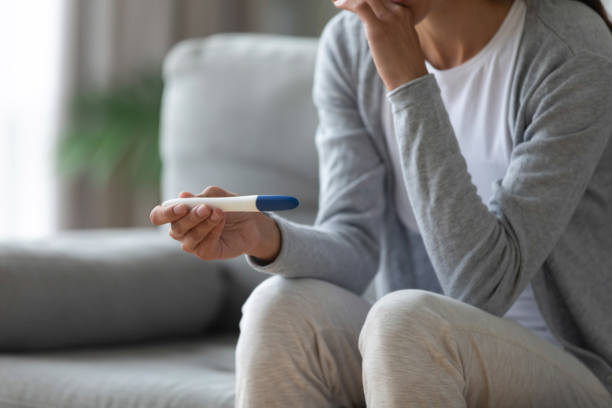 Worried young mixed race woman thinking about possible maternity. Close up thoughtful millennial biracial girl sitting on sofa, holding test in hands, waiting for results. Worried young mixed race woman thinking about possible maternity or unexpected pregnancy. unwanted pregnancy stock pictures, royalty-free photos & images