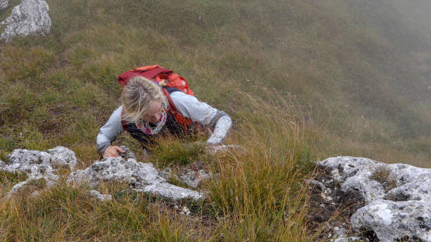 istock Female mountaineer scrambles up grassy cliff 1182206237