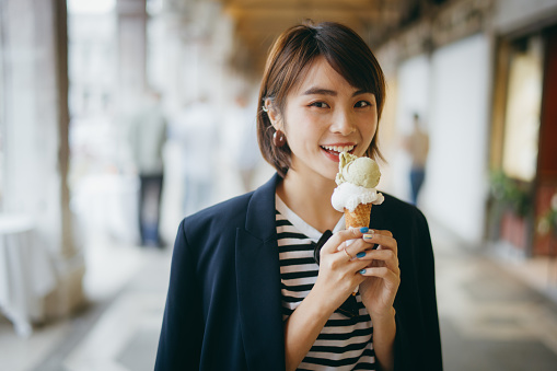 Joyful young Asian female traveller enjoying ice cream while exploring and walking through local city street in Italy