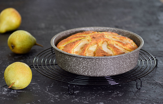 Freshly baked pear cake in a baking dish on a black background.