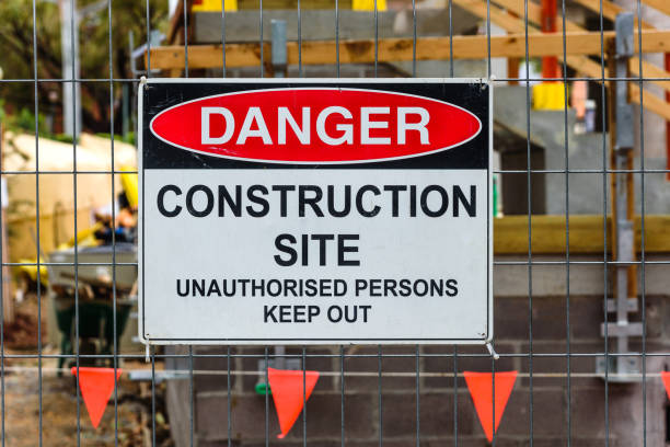 Construction site sign A 'Danger, Construction site, Unauthorised Persons Keep Out' sign mounted on a wire fence in front of a building site fenced area stock pictures, royalty-free photos & images