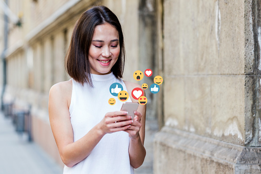 Beautiful Asian woman watching a video live streaming on her phone, emoticons concept