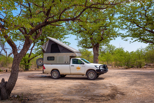 Halali, Namibia - March 27, 2019 : Tent located on the roof of a pickup 4x4 car parked under trees of Halali camp in Etosha National Park.