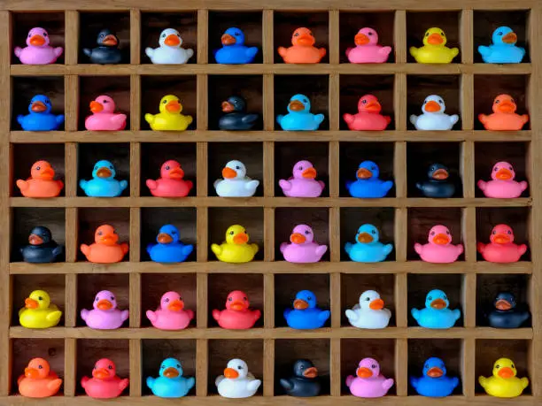 Photo of Many multi-colored rubber ducks in wood pigeon hole compartments.