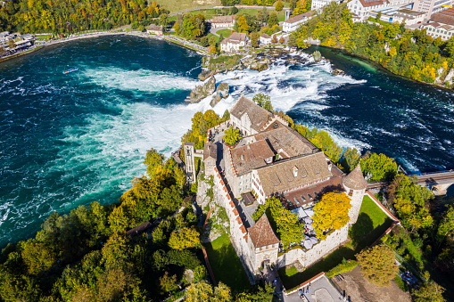 Red roofs and towers of cliff-top Schloss Laufen castle, Laufen-Uhwiesen. Rhine Falls or Rheinfall, Switzerland. Bridge and border between the cantons Schaffhausen and Zürich. Panoramic aerial view.