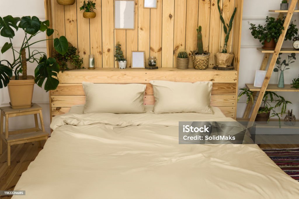 Real photo of a botanical bedroom interior with wooden shelves,  double bed and plants. Bedroom wooden interior with plants next to a bed made with pillows. Headboard Stock Photo