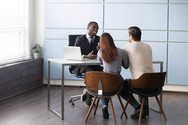 Happy smiling african american male Real Estate Agent consulting young married couple. Happy smiling african american male Real Estate Agent broker banker talking consulting young married couple. Full length millennial family spouse meeting real estate agent or financial advisor at office. bank manager stock pictures, royalty-free photos & images