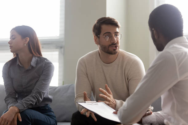 Young dissatisfied woman getting bored while husband talking with psychologist.