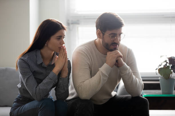 気の毒な女性は、気の毒な夫の近くに座って、申し訳ありません。 - pleading men women reconciliation ストックフォトと画像