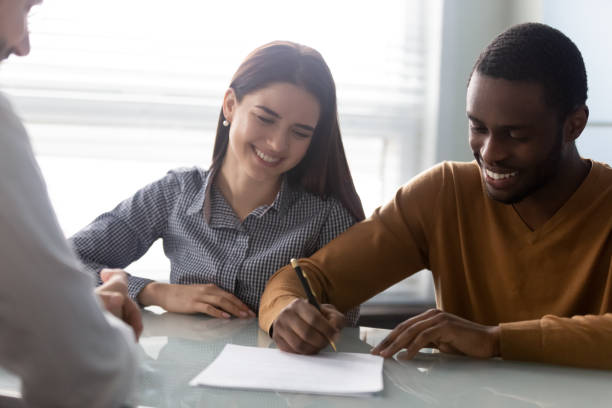 Young smiling woman watching husband signing contract. Head shot young smiling woman watching african american happy husband signing contract at bank worker meeting in office. Satisfied mixed race family couple making agreement, important decision. women satisfaction decisions cheerful stock pictures, royalty-free photos & images