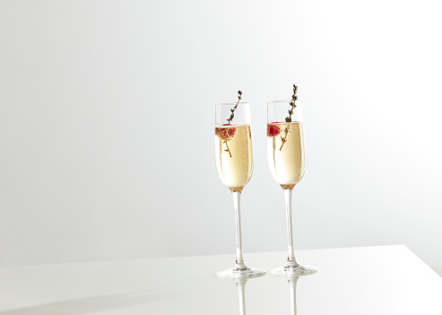 Shot of two champagne glasses with raspberries on a white background
