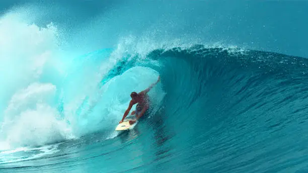CLOSE UP: Young professional surfboarder finishes riding another epic tube wave on a sunny day in French Polynesia. Surfer having fun in the refreshing emerald water on a perfect day for surfing.