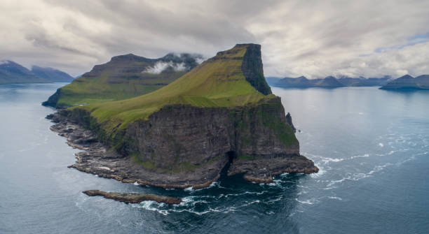istock AERIAL: Tiny white lighthouse close to black cliff looks over the tranquil sea. 1182236507