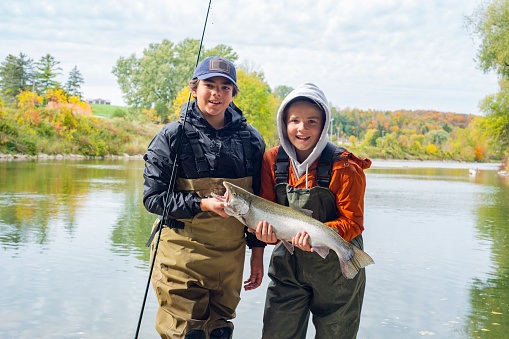 Two young fisherman holding a freshly caught rainbow trout or Steelhead on a fall day.