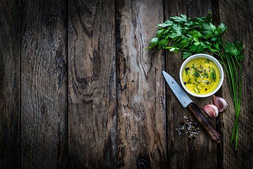 Food backgrounds: parsley, olive oil and garlic, peppercorns and marine salt placed at the right border of a dark rustic table leaving useful copy space for text and/or logo at the center left. A vintage kitchen knife complete the composition. Predominant colors are brown and green. XXXL 42Mp studio photo taken with Sony A7rii and Sony FE 90mm f2.8 macro G OSS lens