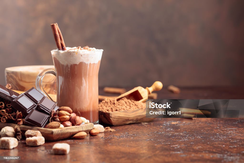 Cokelat panas dengan bubuk kakao, krim, kayu manis, potongan cokelat, dan bahan lainnya di atas meja coklat. - Bebas Royalti Cokelat panas Foto Stok Cokelat panas dengan bubuk kakao, krim, kayu manis, potongan cokelat, dan bahan lainnya di atas meja coklat. - Bebas Royalti Cokelat panas Foto Stok